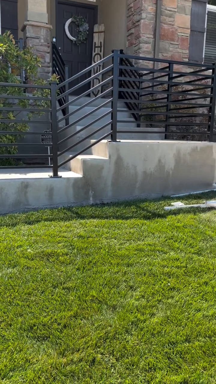 A modern horizontal-picket steel railing on a low concrete wall, powder coated dark
