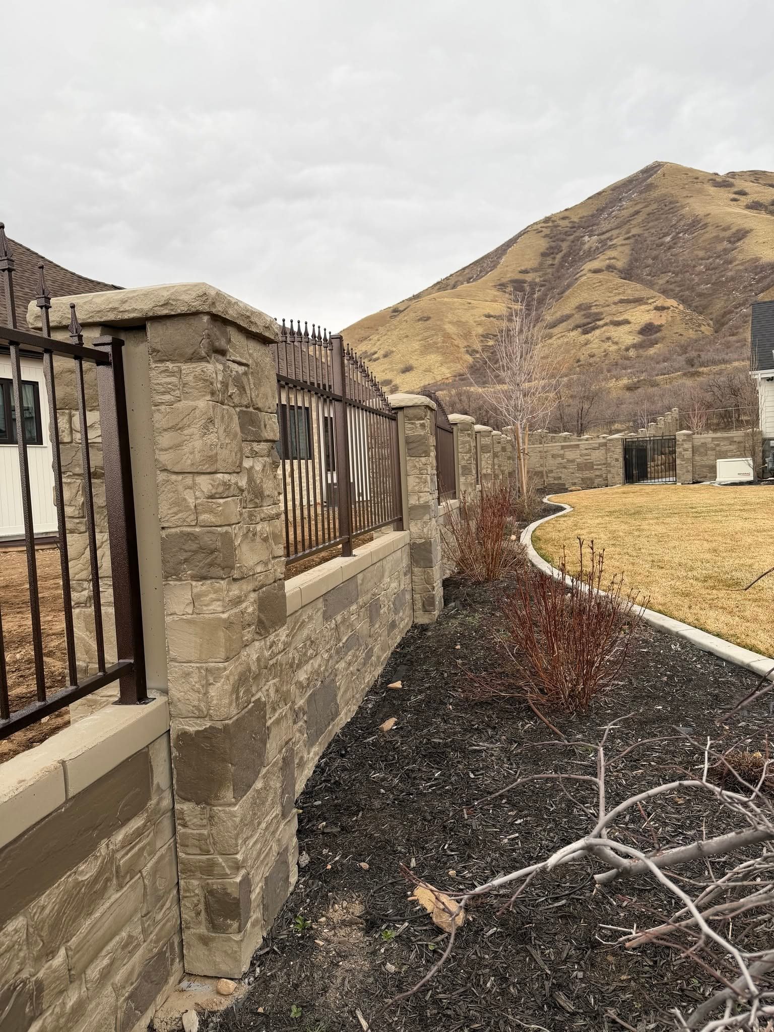 Bronze ornamental iron fence with spear finials set between cut stone columns, running toward the Utah foothills
