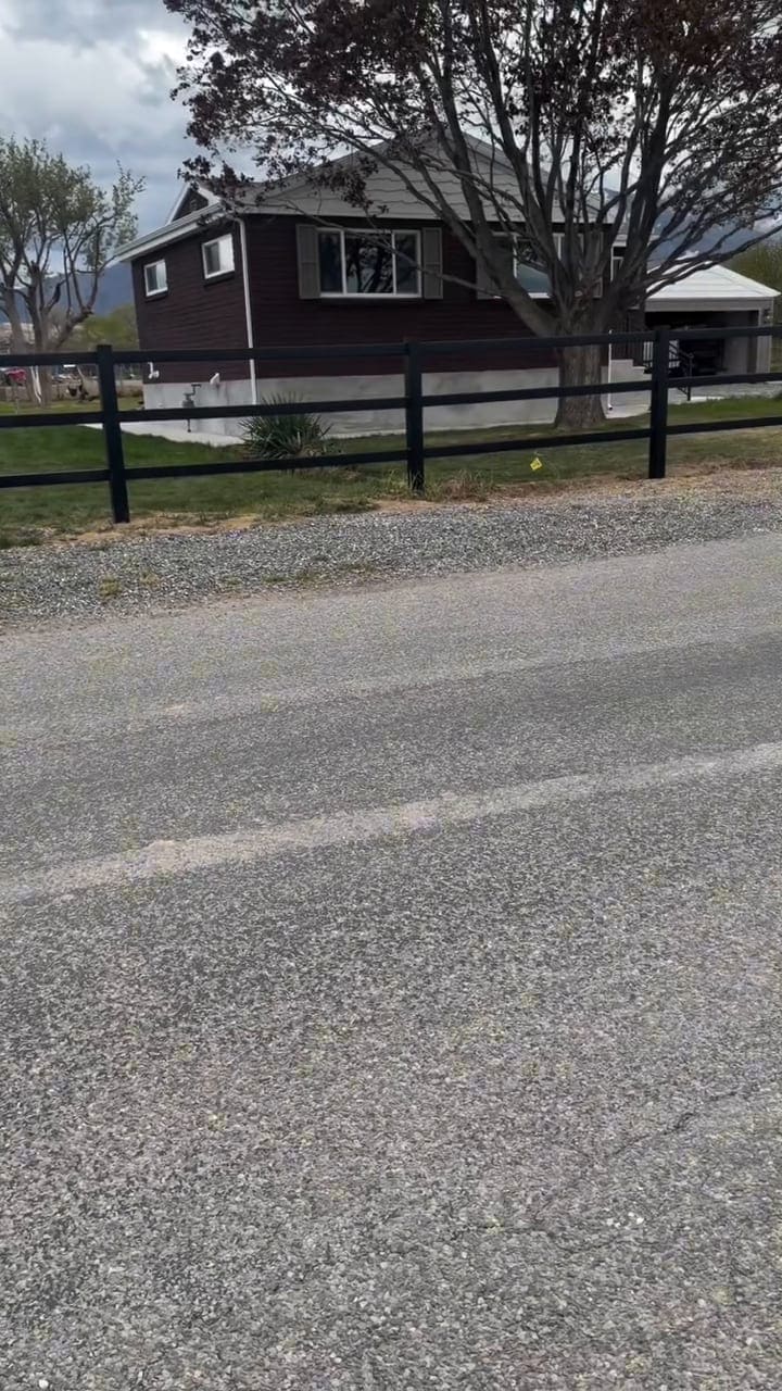 A long black ranch fence running the length of a property beside a road