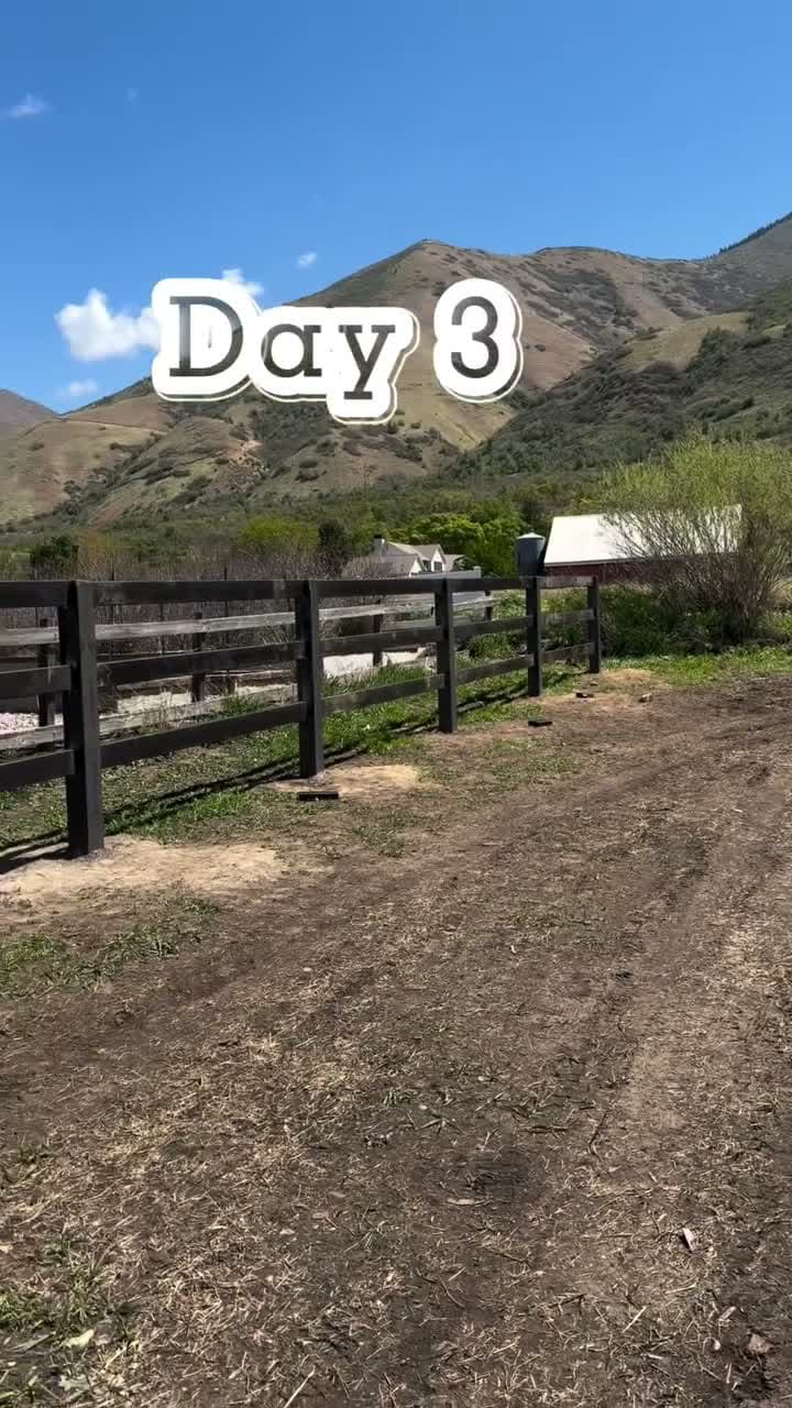 A black ranch fence line running along a dirt track with the mountains behind